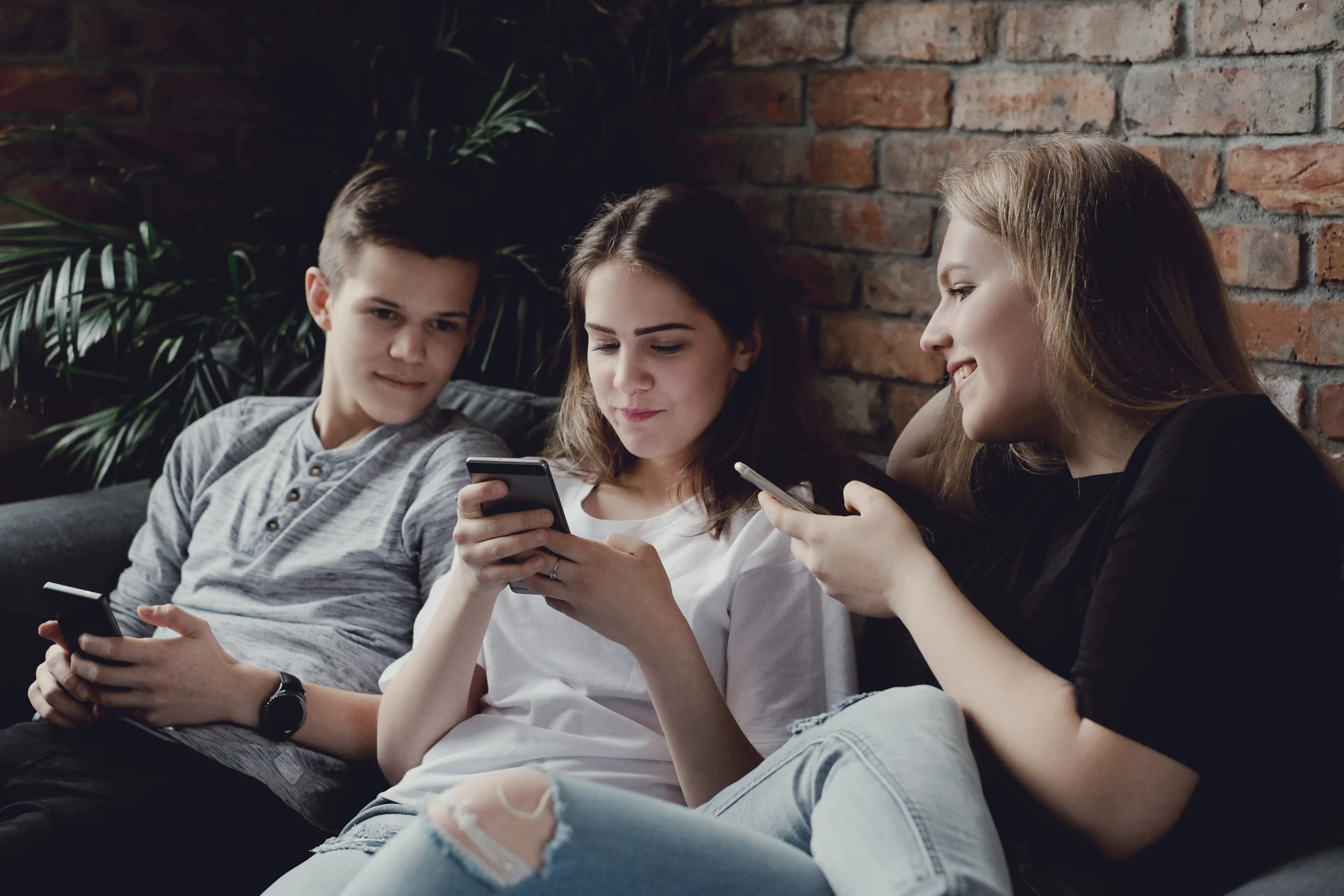 Three people are sitting on the couch and using their smartphones