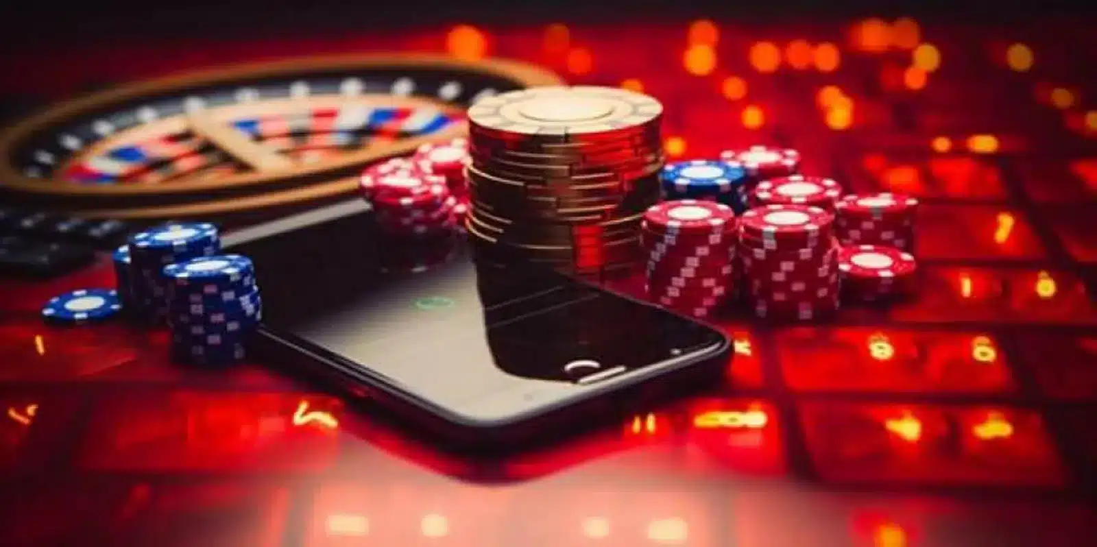 Smartphone on red casino table surrounded by colorful poker chips and a roulette wheel